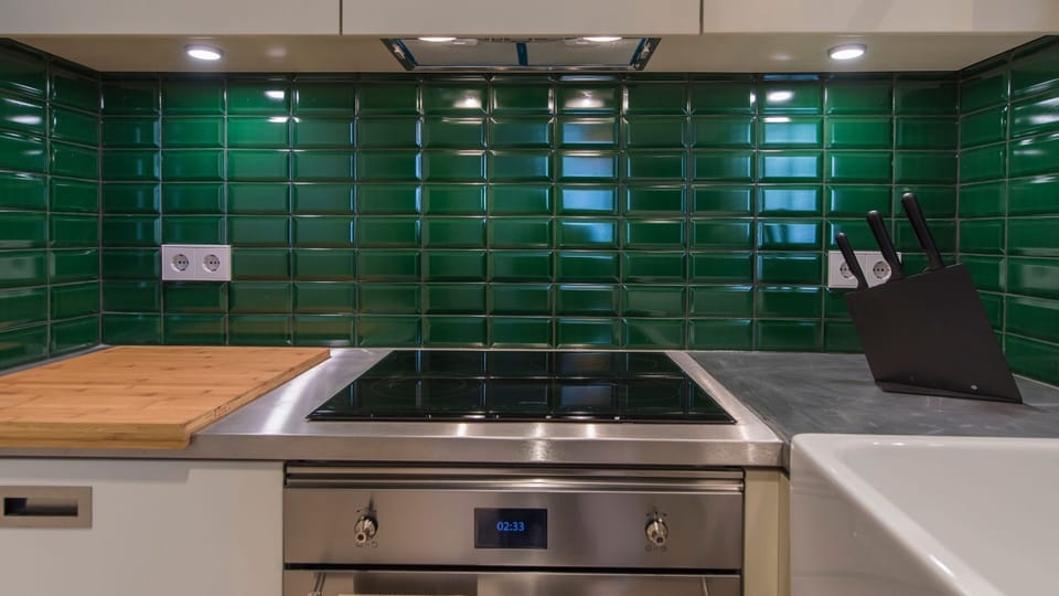 Discover a contemporary kitchen space where preparing meals is a joy, with a clean induction cooktop and stylish green tiled backsplash. Essential utensils are ready for your use, ensuring a convenient and enjoyable cooking experience. #SleekKitchen #Indu