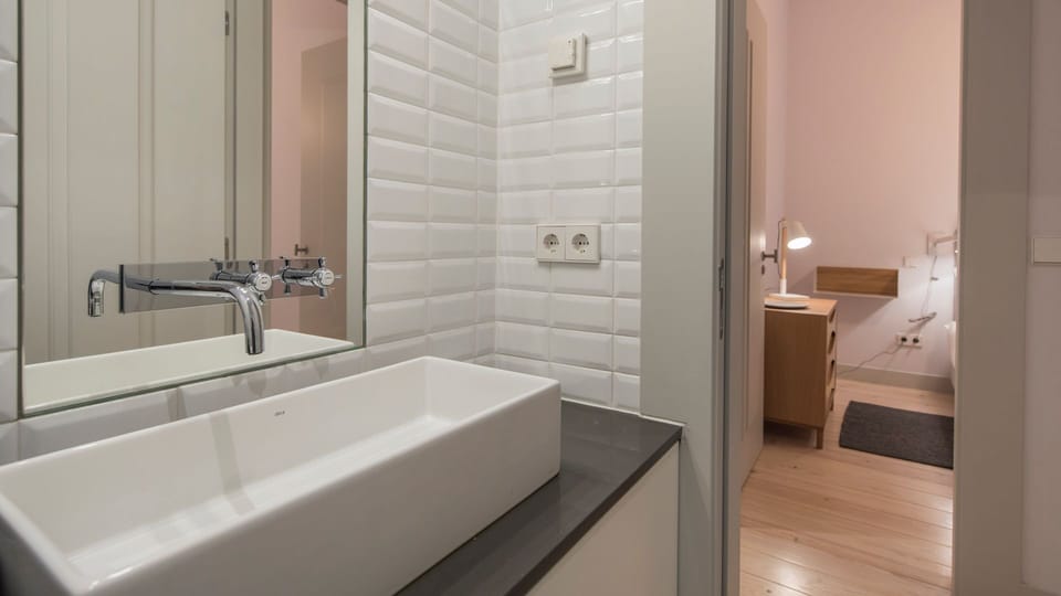 Refresh yourself in the sleek bathroom, featuring a modern vessel sink and bright white subway tiles, ready to invigorate you for the day ahead or soothe you after exploring. A glimpse into the adjacent room suggests a cozy bedroom nearby, ensuring conven