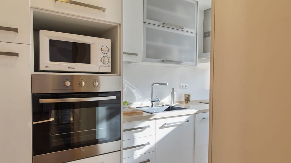 This sleek, fully equipped kitchen boasts modern appliances including an oven and microwave, providing everything needed for delightful culinary adventures. Sunlight streams onto the pristine countertops.