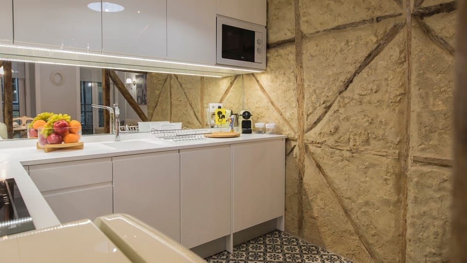 Prepare your morning coffee or a delicious meal in this sleek, fully equipped kitchen, where modern design meets historic charm with its unique exposed stone wall. The reflective backsplash and under-cabinet lighting create a bright and inviting space, pe