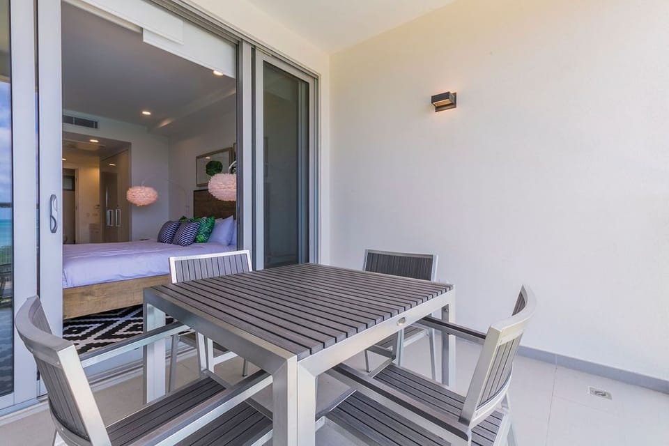 Your private terrace invites morning coffee or evening cocktails at a sleek dining set, just steps from your cozy bedroom with its sliding glass doors open wide.