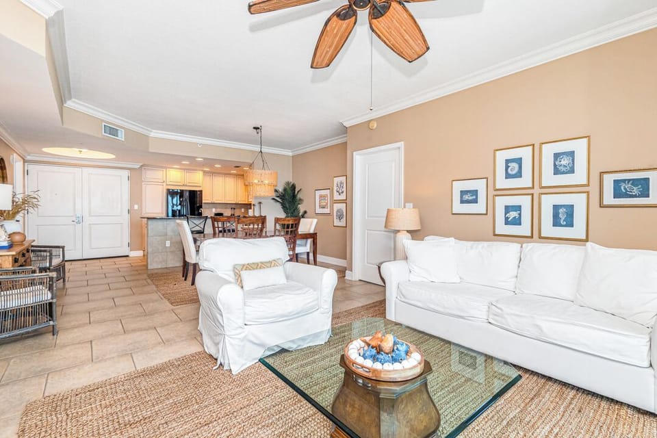 Sink into plush white sofas beneath wooden ceiling fans in this bright, open living space that flows effortlessly into the dining area and kitchen—perfect for gathering with loved ones.