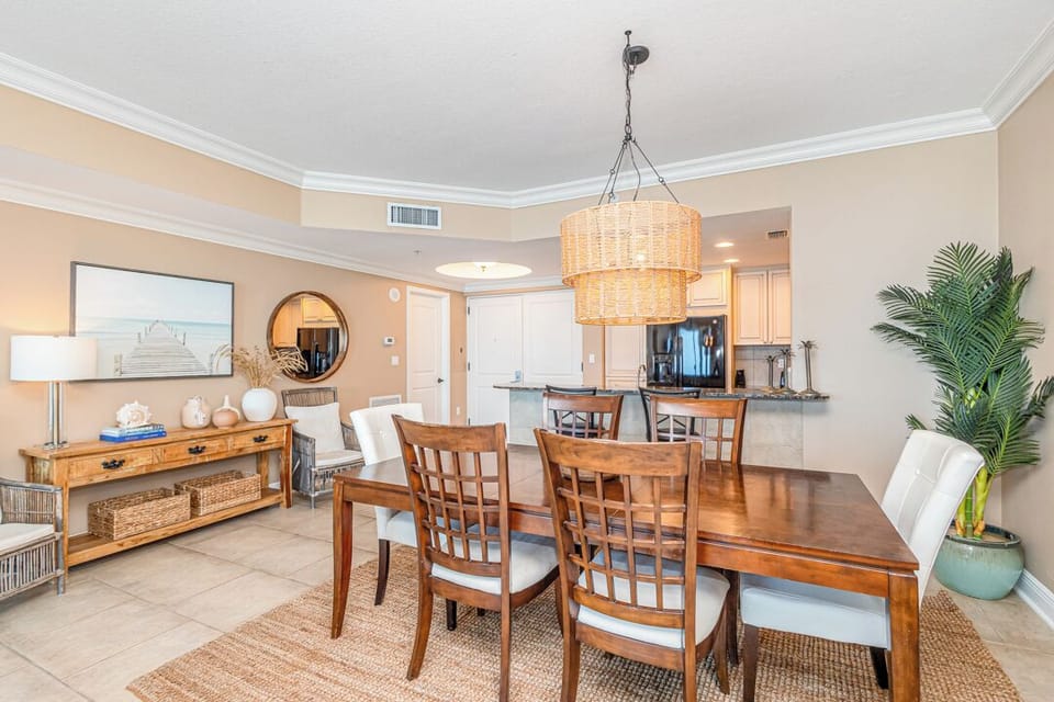 Gather around the warm wood dining table under coastal-inspired lighting, where shared meals and conversations become cherished vacation memories in this inviting open-plan space.