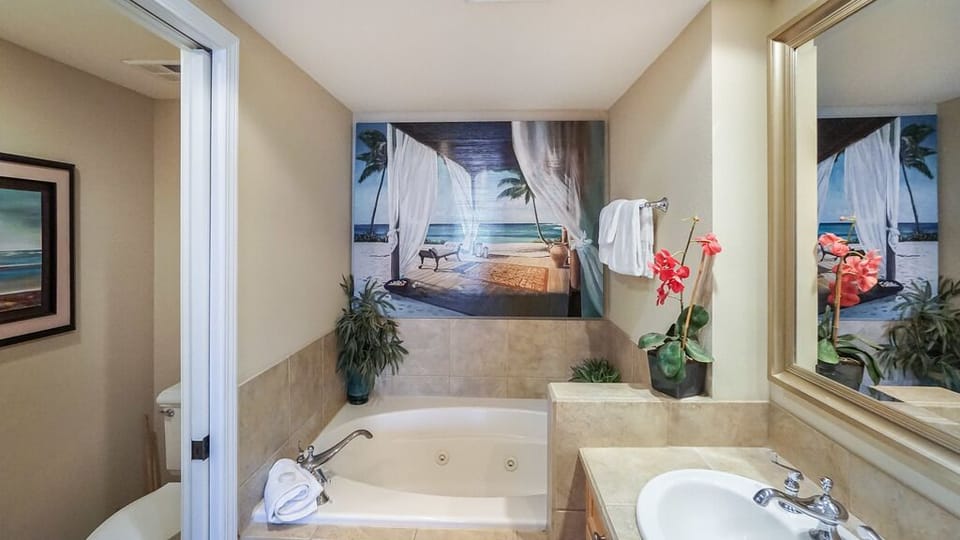 Slip into your own private spa retreat—crisp white linens await on the jet tub, tropical blooms add a pop of color, and the serene artwork above invites you to unwind in luxurious calm.