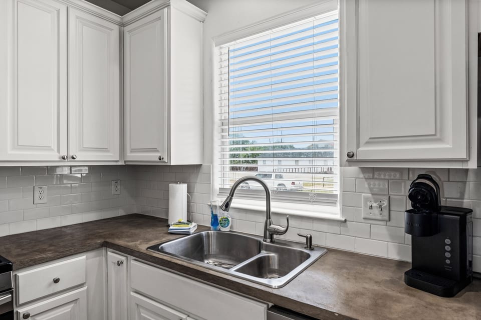 Kitchen sink and counter space at Summer Bliss — dark countertops, deep sink, Keurig coffee maker, and natural light from the window. Morning coffee sorted.