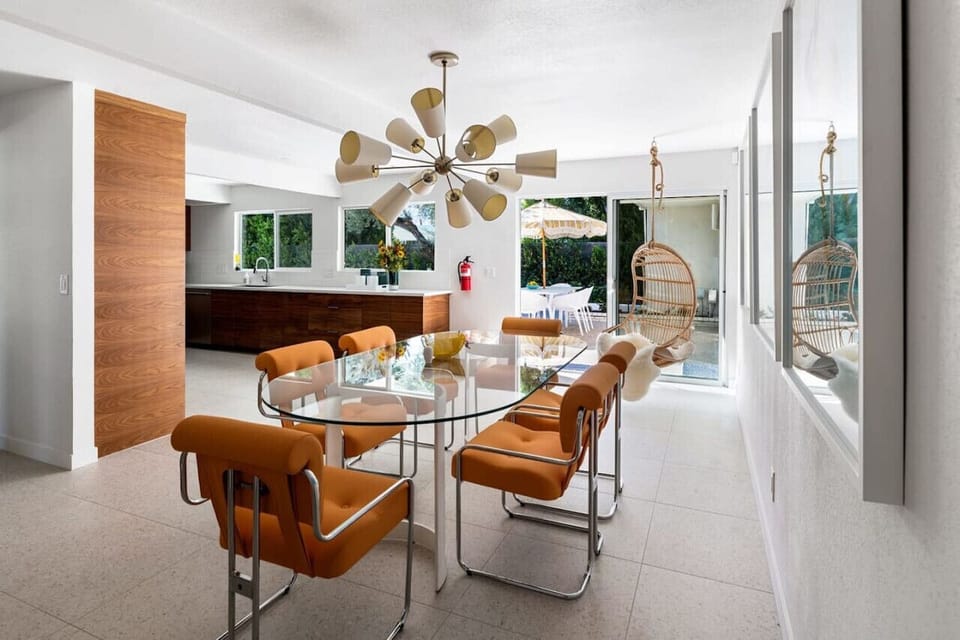 A dream dining setup – stylish orange chairs, a statement chandelier, and seamless indoor-outdoor flow.