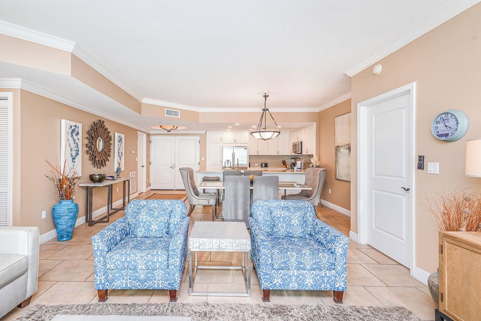 Sink into coastal comfort in your elegantly furnished living space, where blue patterned chairs and warm peach walls create a relaxing atmosphere.