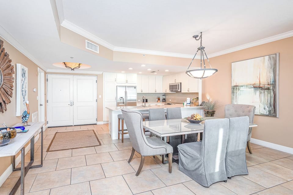Your open-concept space flows seamlessly from kitchen to dining, where elegant blue chairs invite leisurely meals under coastal artwork.