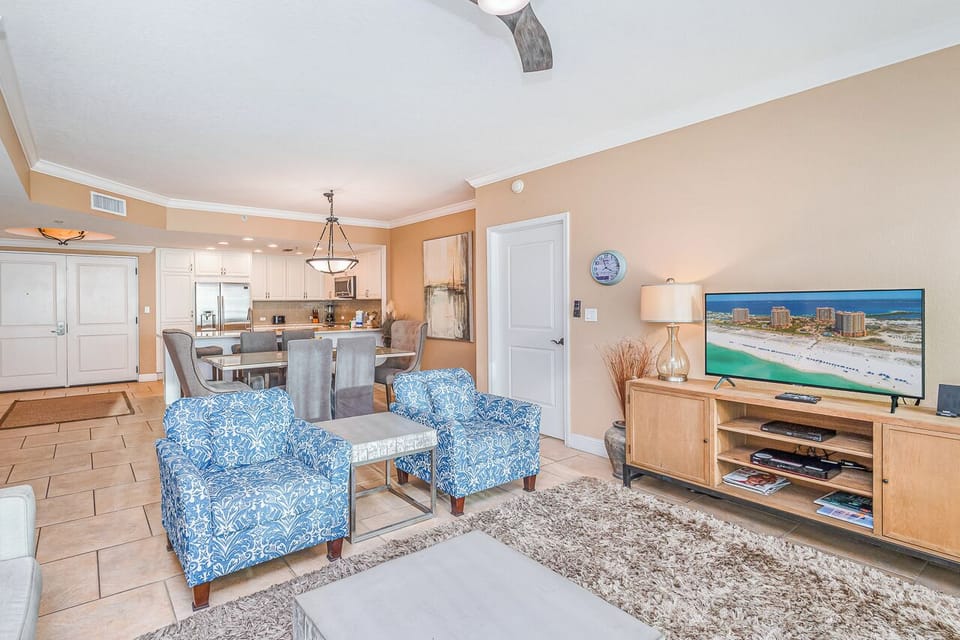 Sink into coastal comfort with your open-plan living space featuring vibrant blue armchairs and modern kitchen—perfect for beach vacation relaxation.