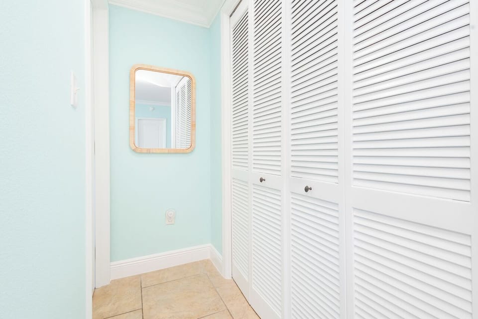 Step into your charming coastal-themed entrance with calming mint walls and ample storage behind elegant louvered doors.