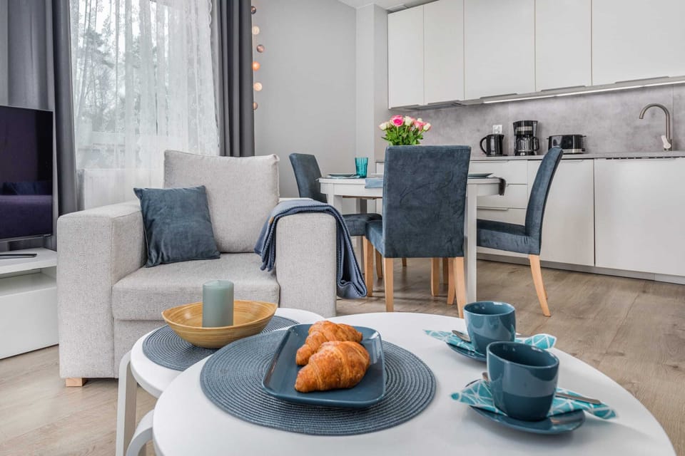 A close-up of a coffee table with a plate of croisants and cups. In the background you can see a soft, light armchair from which you can watch TV.