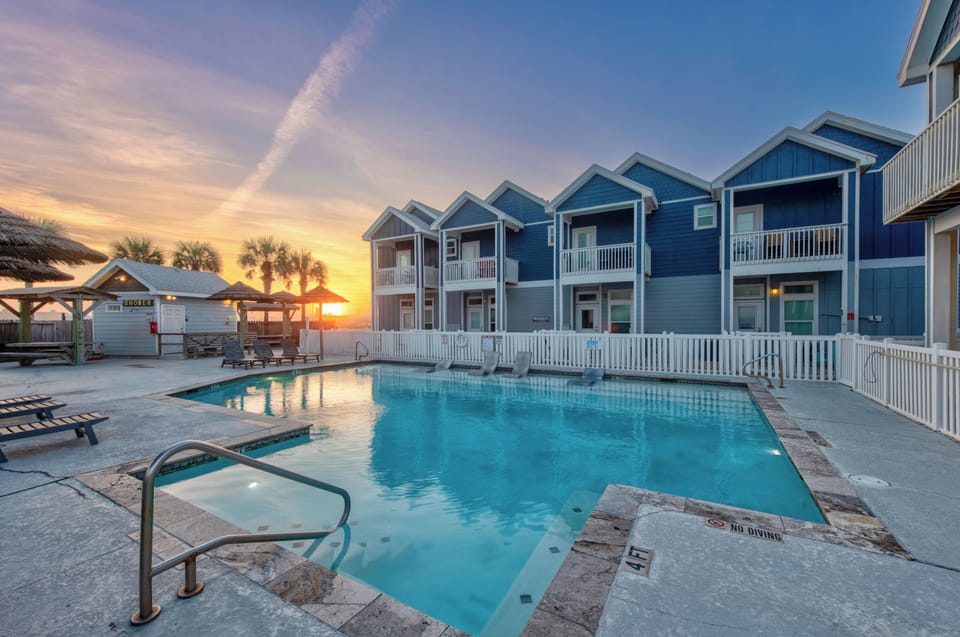 Stunning coastal retreat with colorful beach houses overlooking a sparkling pool area during golden hour sunset.