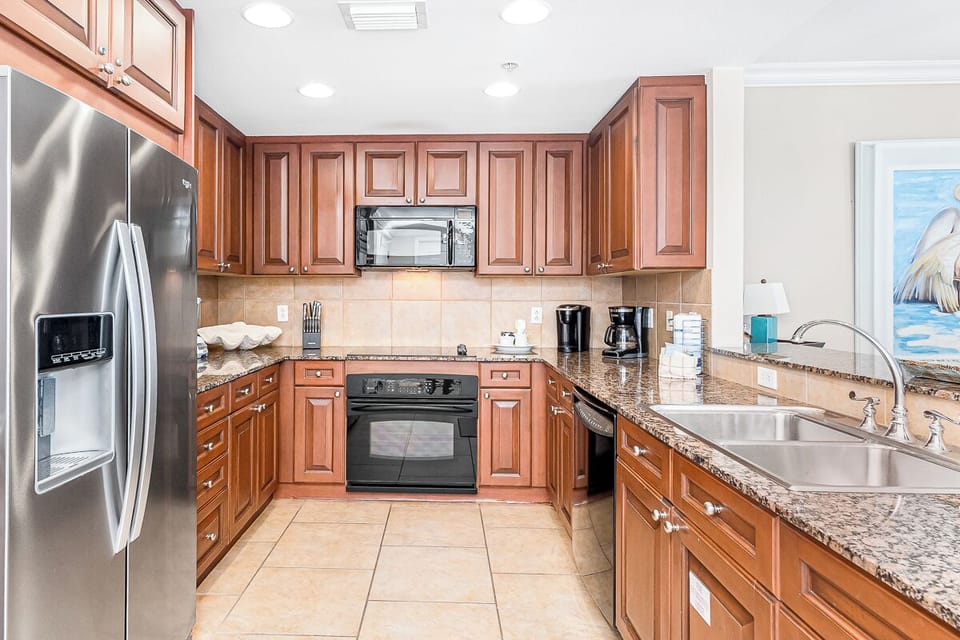 Your fully equipped kitchen awaits with granite counters, stainless appliances, and rich wood cabinets—perfect for preparing meals with coastal views.