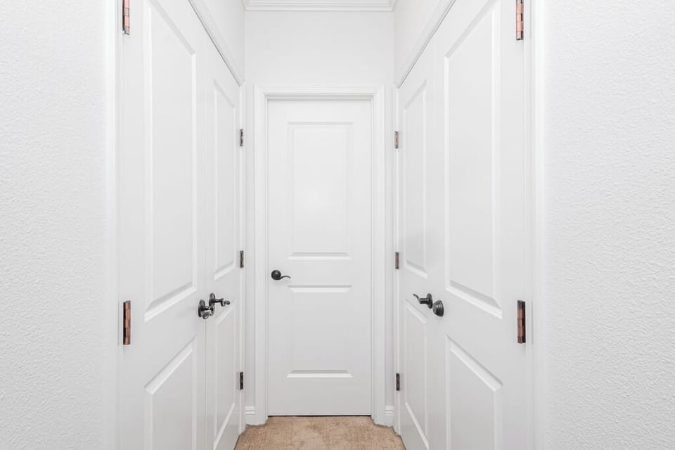 Clean, bright hallway with three bedroom doors and warm leather handles—your private retreat is just beyond these elegant entryways.