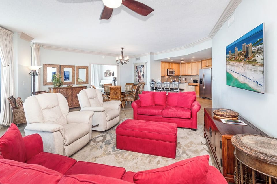 Unwind in your spacious living room, where vibrant coral sofas and plush recliners invite you to relax. The open layout flows into the dining area and modern kitchen—perfect for gathering.