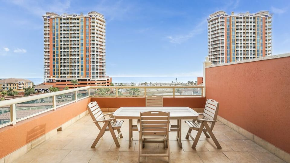 Your private terrace offers outdoor dining space with seating for four, framed by sunny skies and glimpses of palm-lined surroundings—perfect for morning coffee or evening meals in the warm air.