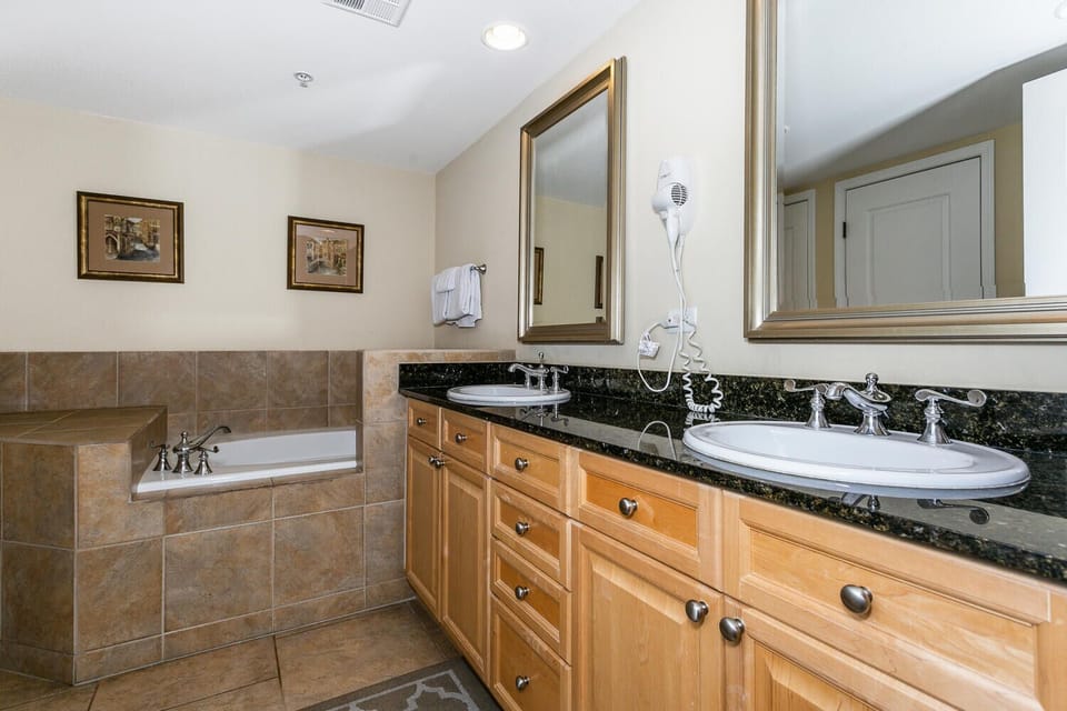Unwind in this elegant bathroom featuring a deep soaking tub and dual vanities with polished granite countertops. The warm wood cabinetry and soft lighting create your perfect retreat after a day of adventure.