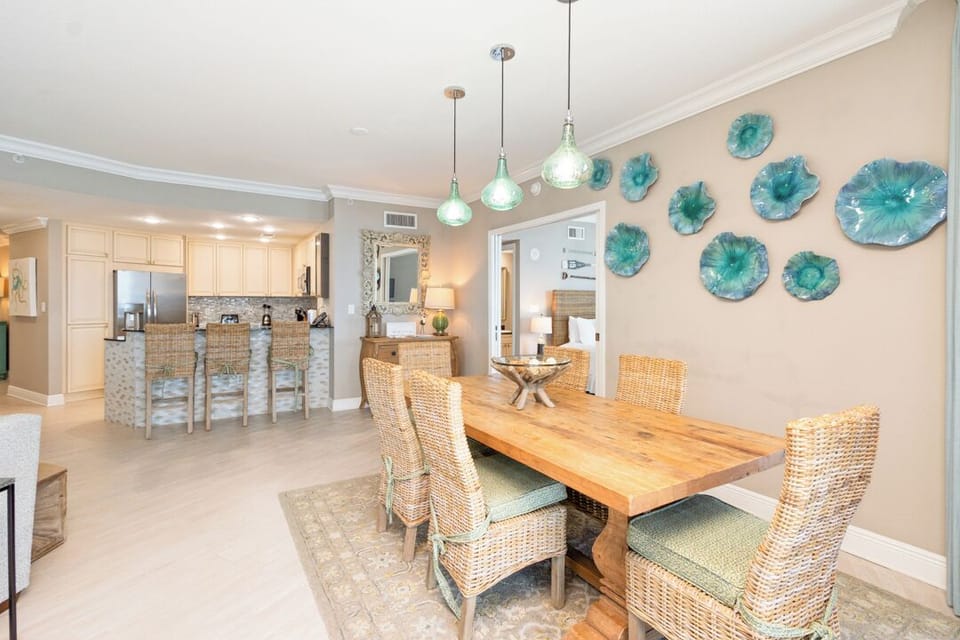 Gather with your group around this beautiful wooden dining table under coastal-inspired pendant lights, with turquoise wall art setting a relaxed, beachy tone throughout your open-concept space.