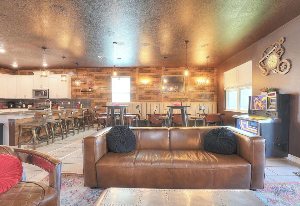 A spacious open-concept living room designed in a steampunk aesthetic, featuring a dining area reminiscent of a restaurant with crocodile leather booths and tables for over 16 guests, plus 6 counter stools at the kitchen bar.