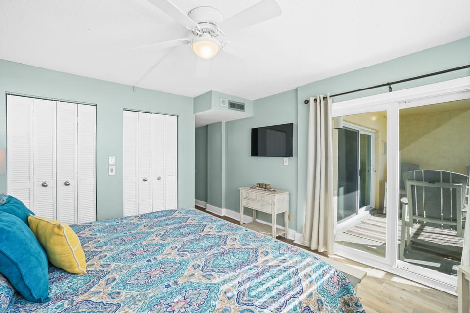 Master bedroom with a king bed, smart TV, ceiling fan, and a private entrance to the balcony, plus a window to look out at the beach!
