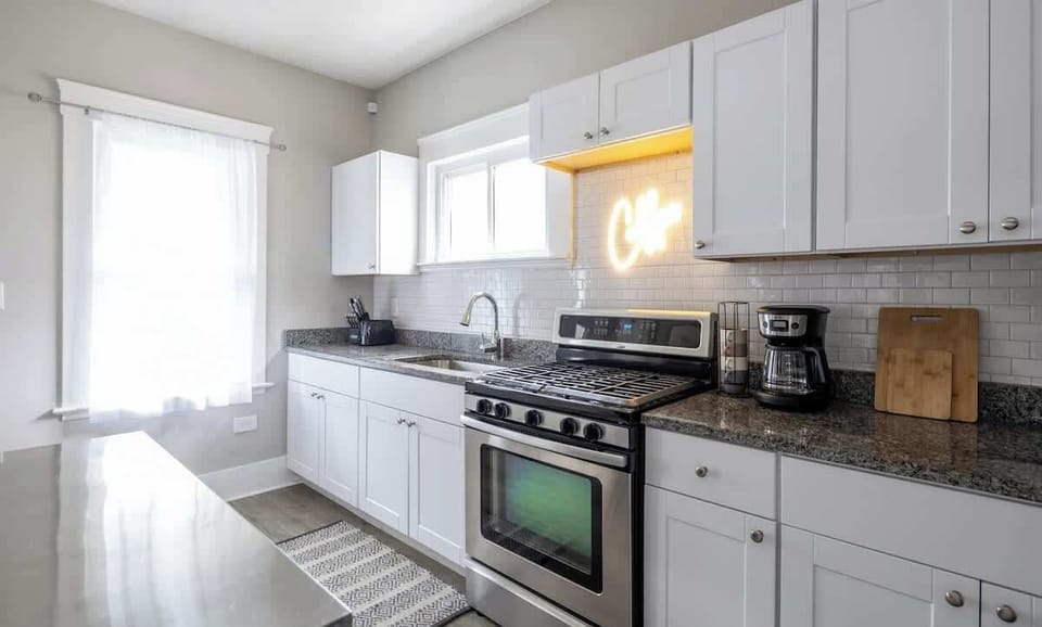 Clean kitchen w/ white cabinets, stove & window bringing in soft daylight