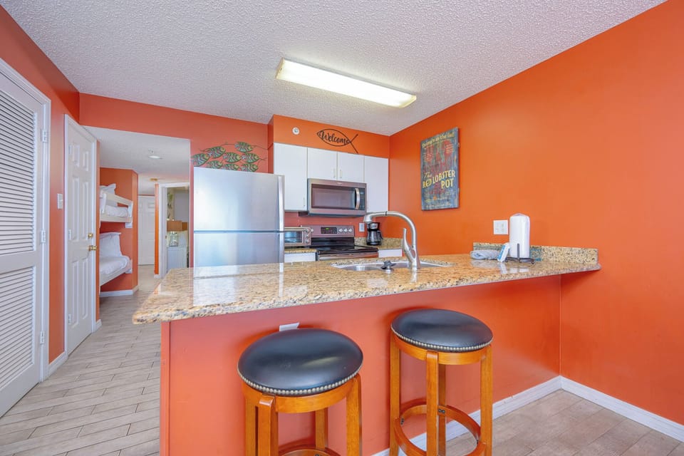 The kitchen features vibrant walls, granite countertops, stainless appliances, and bar seating for a cheerful experience