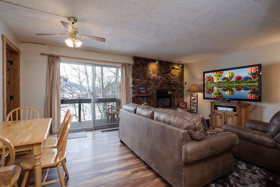 Your spacious living room invites relaxation with plush leather seating, a cozy stone fireplace, and large windows revealing peaceful winter views.