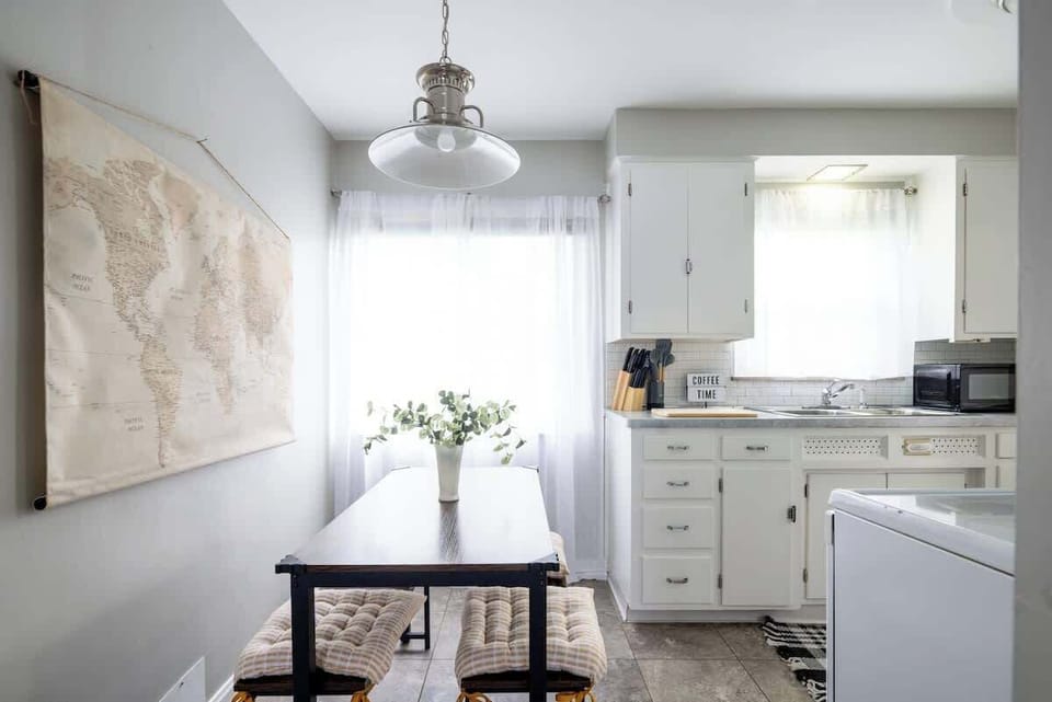 - Bright Airbnb kitchen with dining nook and storage   - Modern details with functional cooking essentials   - White cabinetry and clean design for guest comfort