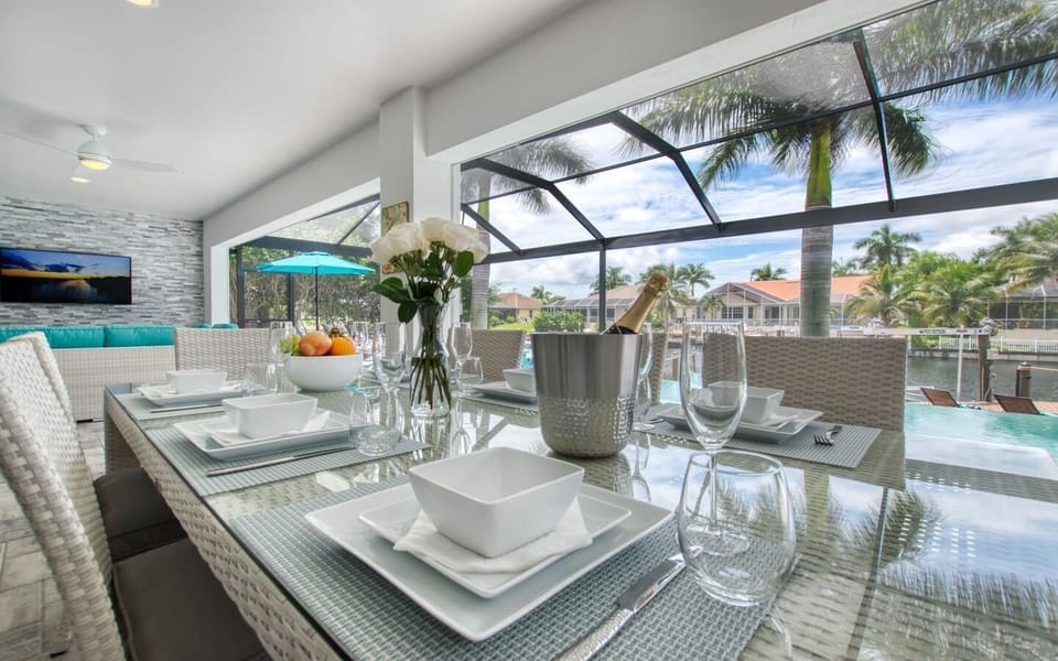 Outdoor dining table set with plates, glassware, and a centerpiece arrangement under the screened enclosure