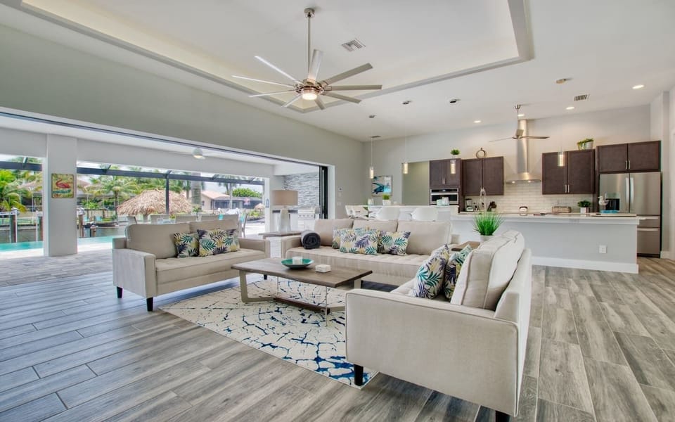 Open-concept living and dining area with modern furnishings, ceiling fan, and natural light from large windows