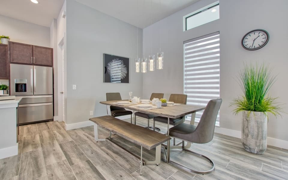 Dining table with modern chairs, overhead pendant lighting, and kitchen visible in the background