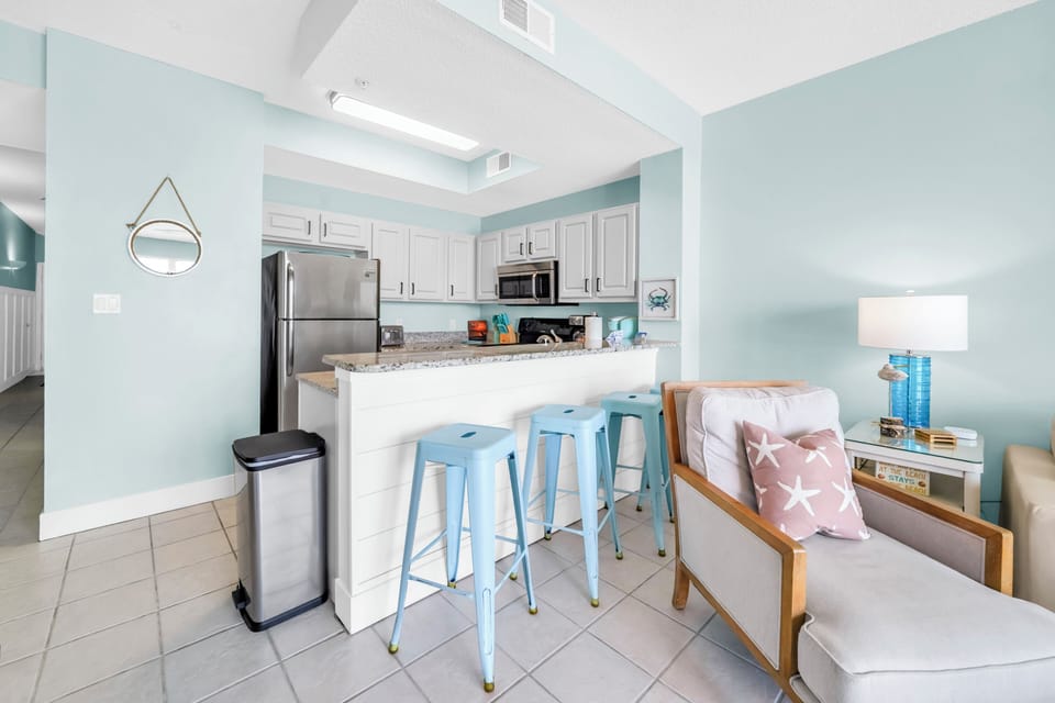 Your coastal-themed kitchen invites culinary adventures with modern appliances, breakfast bar seating, and soothing seafoam walls that make meal prep feel like vacation.