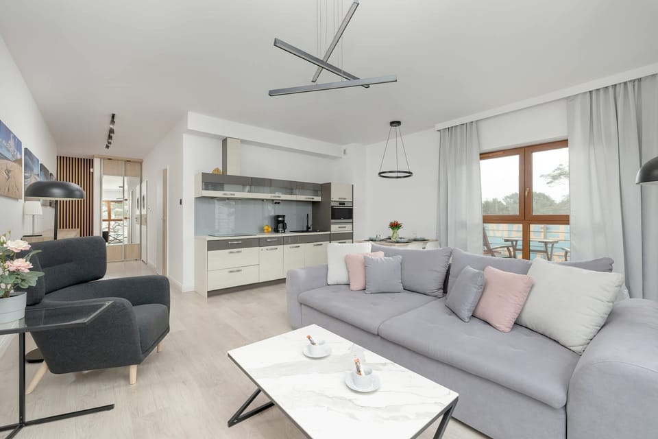 A bright and modern living room featuring a light gray sofa, a sleek black armchair, and a coffee table, with large windows letting in abundant natural light.
