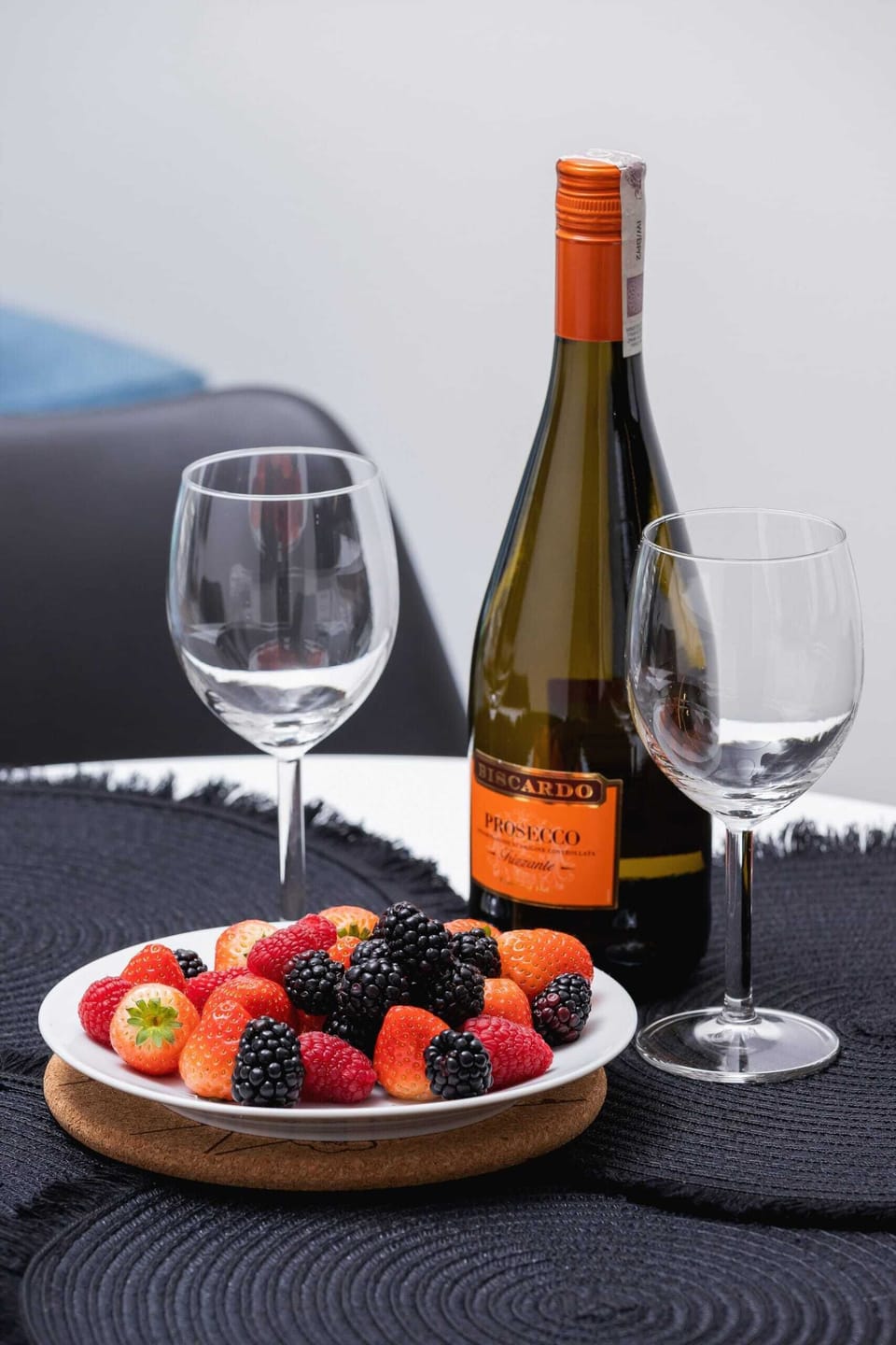 A table setup with a bottle of wine, a glass, and a plate of berries, suggesting a luxurious meal setting.