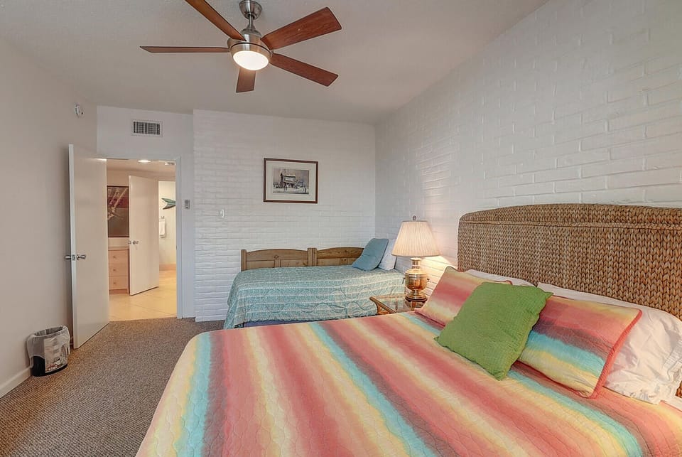 Drift into comfort in your airy bedroom, where colorful bedding meets coastal charm and gentle ceiling fan breezes create your perfect retreat.