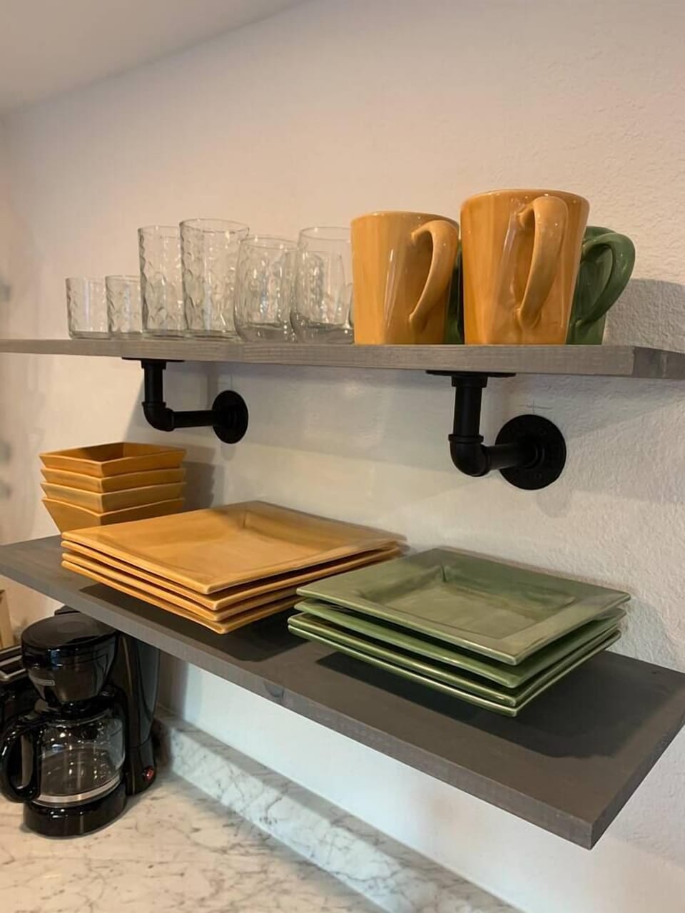 This close-up shot of the studio's open shelving highlights a set of modern, square ceramic plates in earthy tones of mustard and sage.