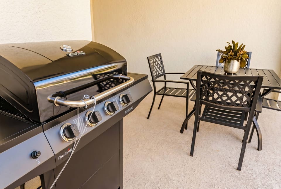 Covered outdoor area with a grill and dining table for four, perfect for preparing meals and enjoying relaxing moments outdoors with family.