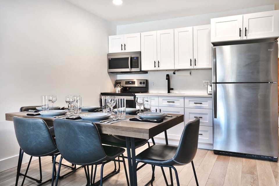 Dining room with wooden table, gray leather barrel dining room chairs, and kitchen in the background