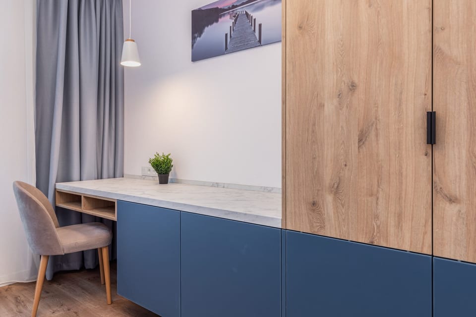 A small work area in the bedroom, featuring a wooden desk, a blue drawer, and a chair.