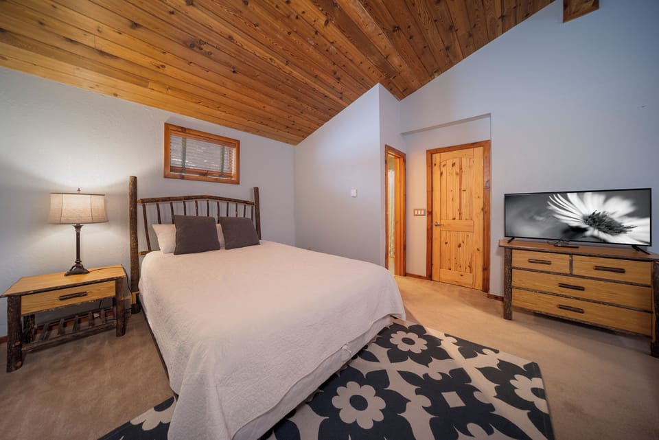 Rest peacefully in your rustic bedroom with exposed wood ceiling beams, cozy furnishings, and modern amenities for the perfect mountain retreat experience.