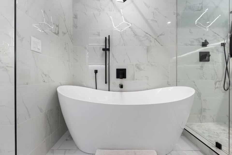 Freestanding tub surrounded by sleek marble tile and matte black fixtures.

