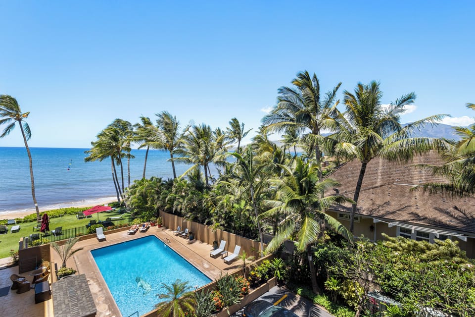 Stunning beachfront property featuring a sparkling pool nestled among swaying palms, where the ocean meets lush tropical gardens and inviting lounge chairs await under endless blue skies.