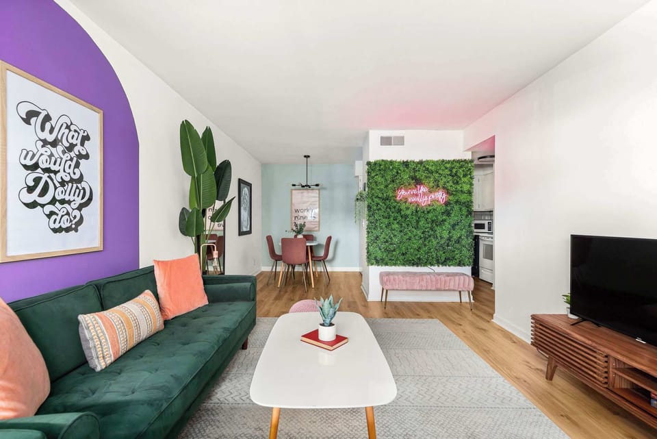 Bright living room with velvet sofa, neon wall art, and open dining table.