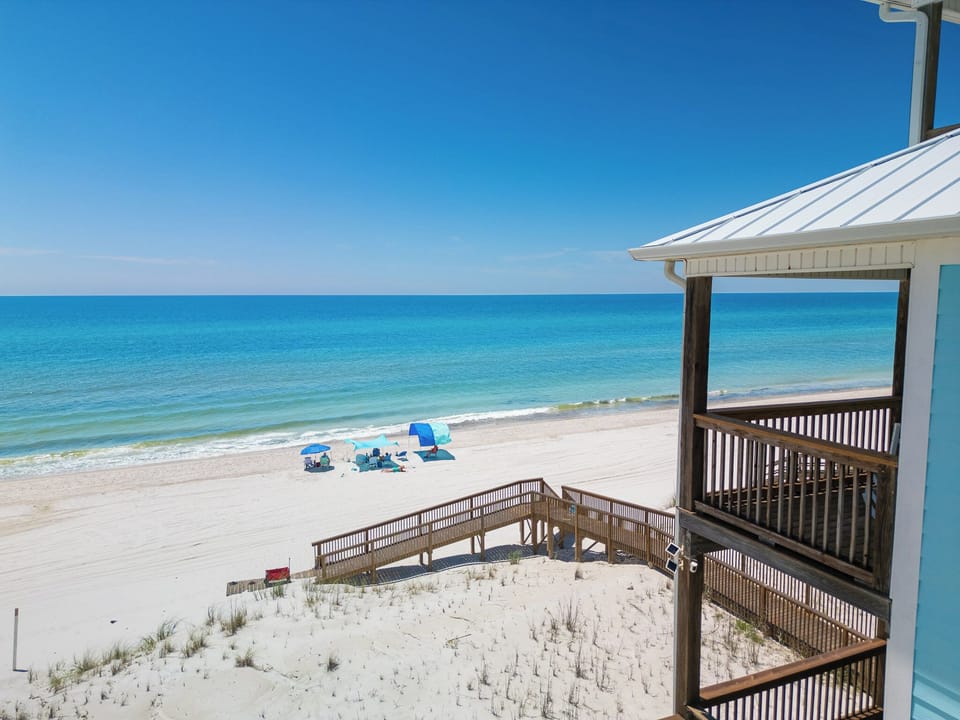 A beachside property on Florida's Gulf Coast offers direct access to pristine white sand and turquoise waters under clear blue skies.