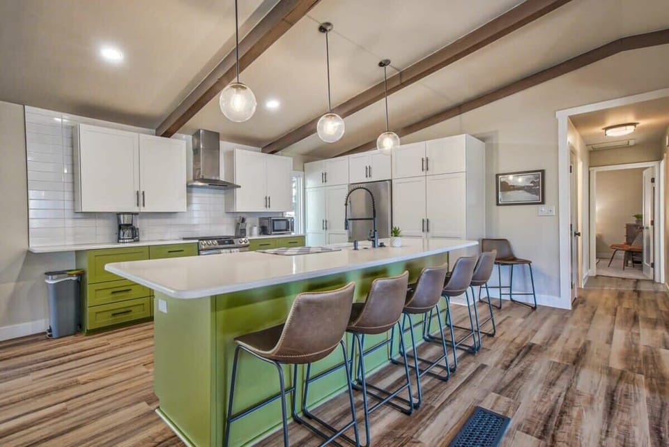 A long kitchen island with a bold green base and barstool seating invites everyone to gather while meals come together. Pendant lights hang overhead and the open layout keeps the conversation flowing from prep time to shared bites.