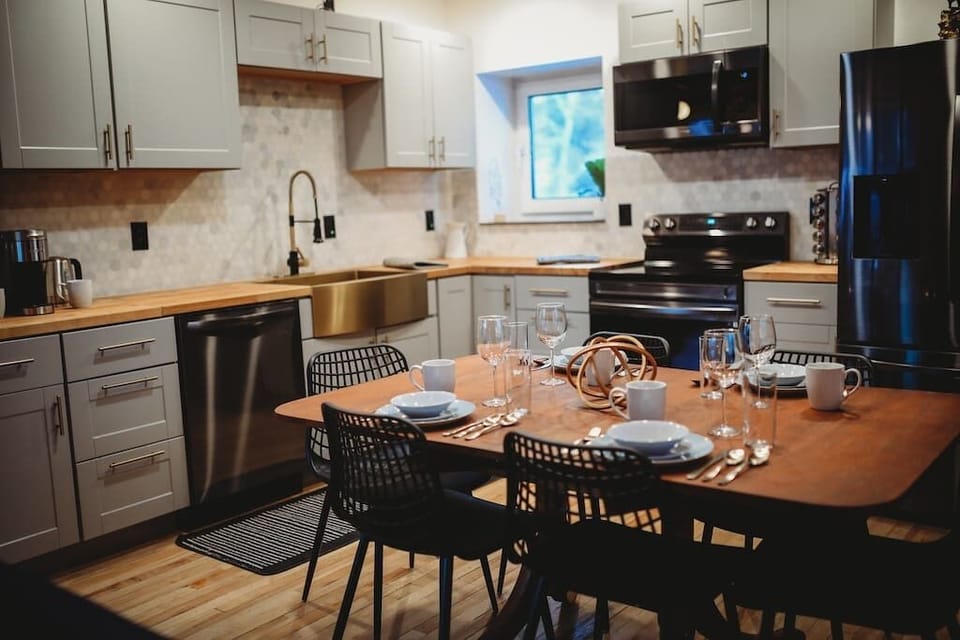 A sleek log cabin kitchen with gray cabinets, stainless-steel sink, and modern appliances. Adjacent is a cozy dining area with a wooden table and black chairs.