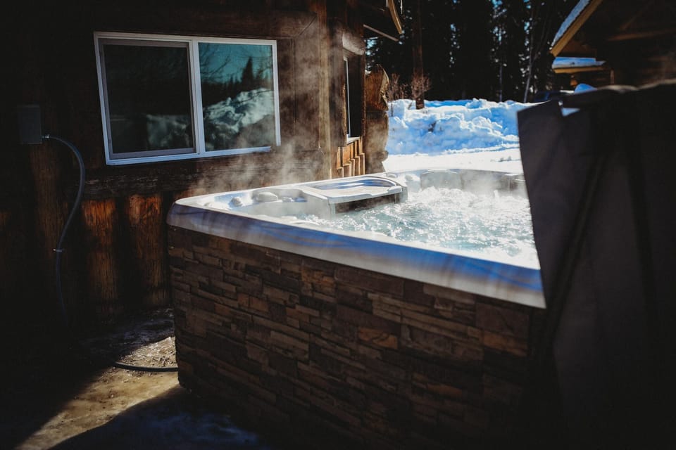 An outdoor hot tub surrounded by snow, exuding warmth and relaxation. The hot tub's steam contrasts with the frosty environment, creating a serene winter retreat.