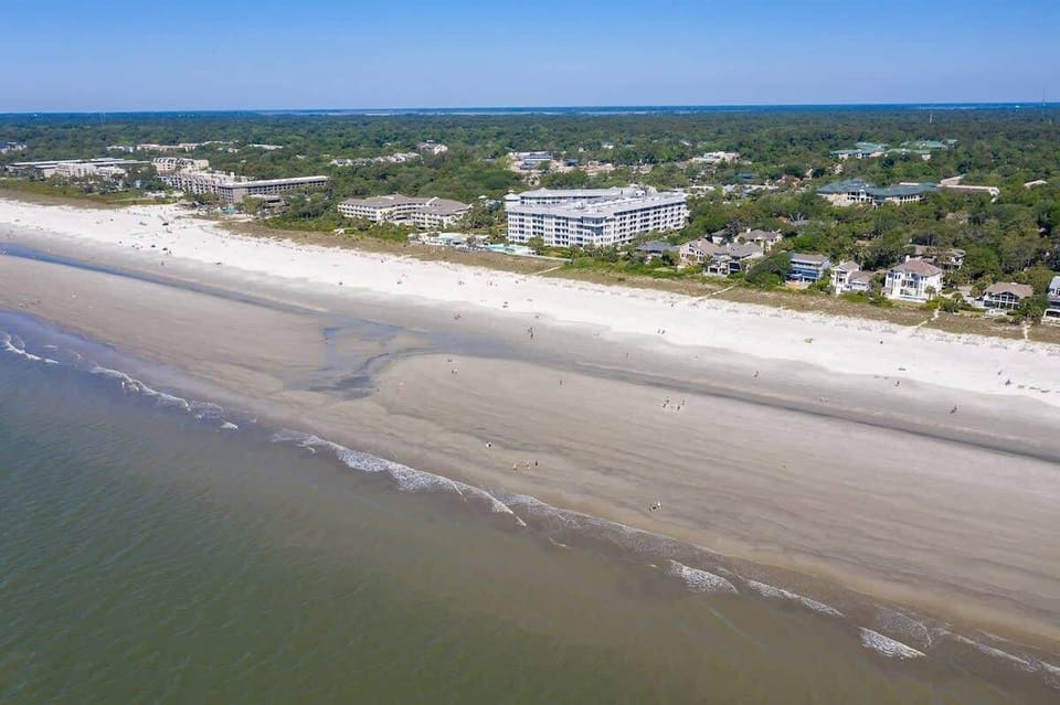Aerial view of a spacious beach with nearby residential and resort buildings.