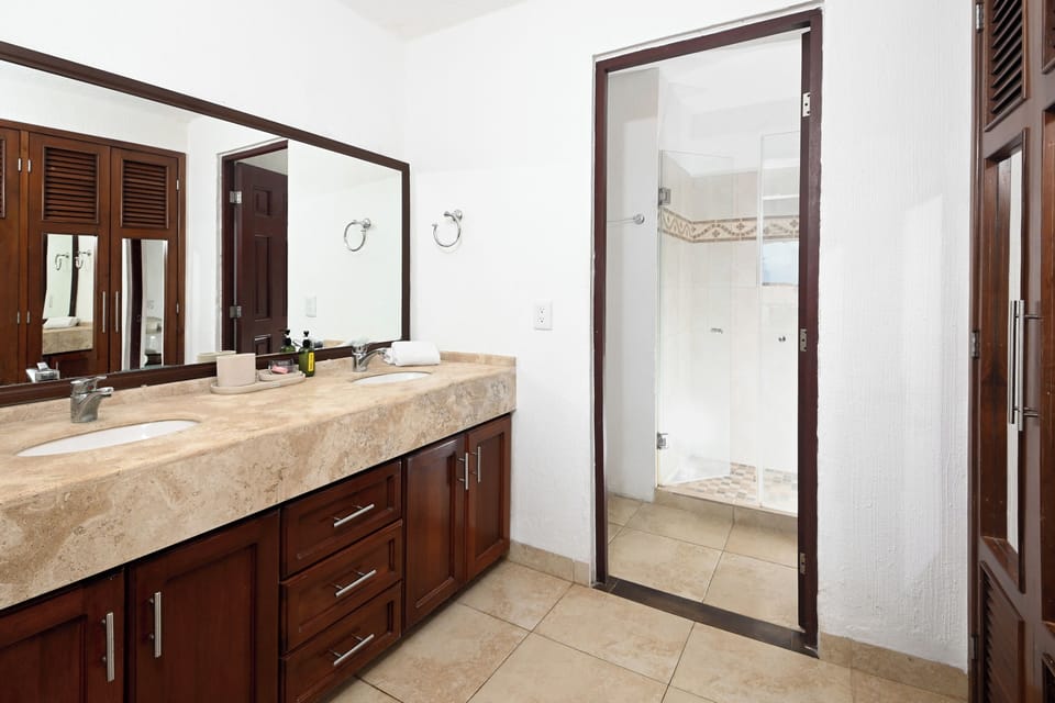 Step into your private bathroom with elegant marble countertops, rich wood cabinetry, and a spacious walk-in shower with decorative tiling—designed for your comfort and relaxation.