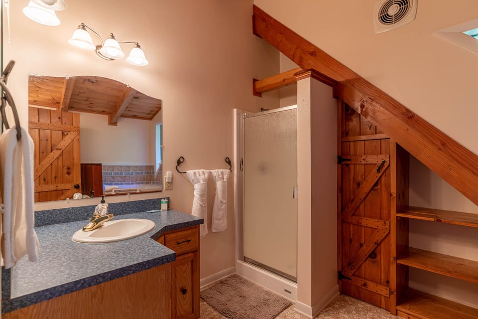 Rustic charm meets comfort in this full bath at Whispering Ridge Retreat, with warm wood beams and a walk-in shower tucked under the staircase.